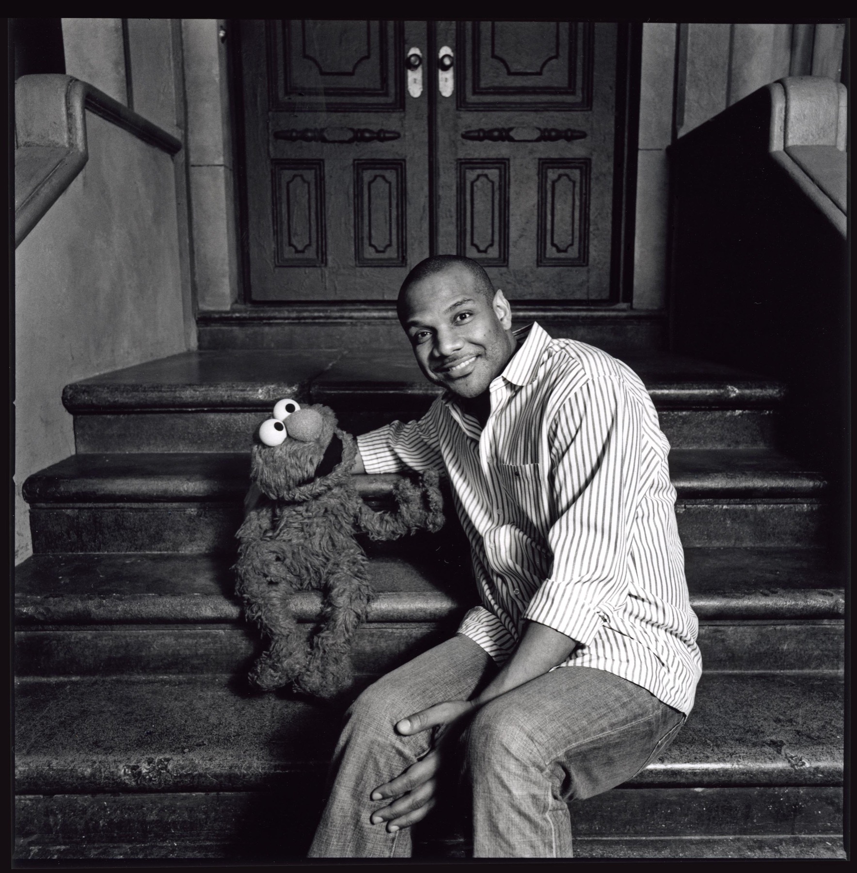 Kevin Clash seated beside Elmo on a city stoop